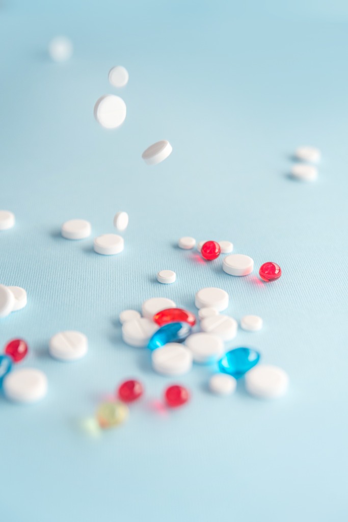 Assorted pharmacy medications including white tablets, red and blue capsules on a light blue background - Platinum Pharmacy UK